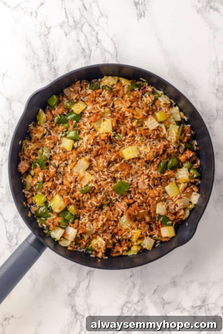 Dirty rice mixture in a skillet, with spices and rice toasted before adding liquid.