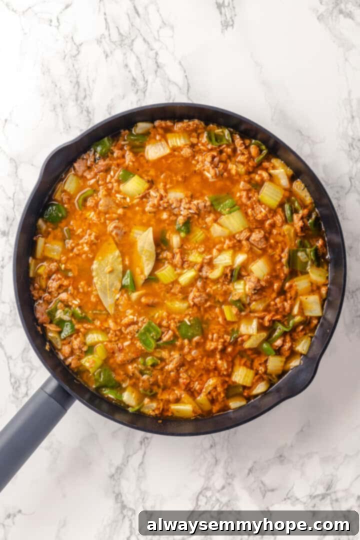 Dirty rice in skillet after adding vegetable stock and bay leaves, simmering.