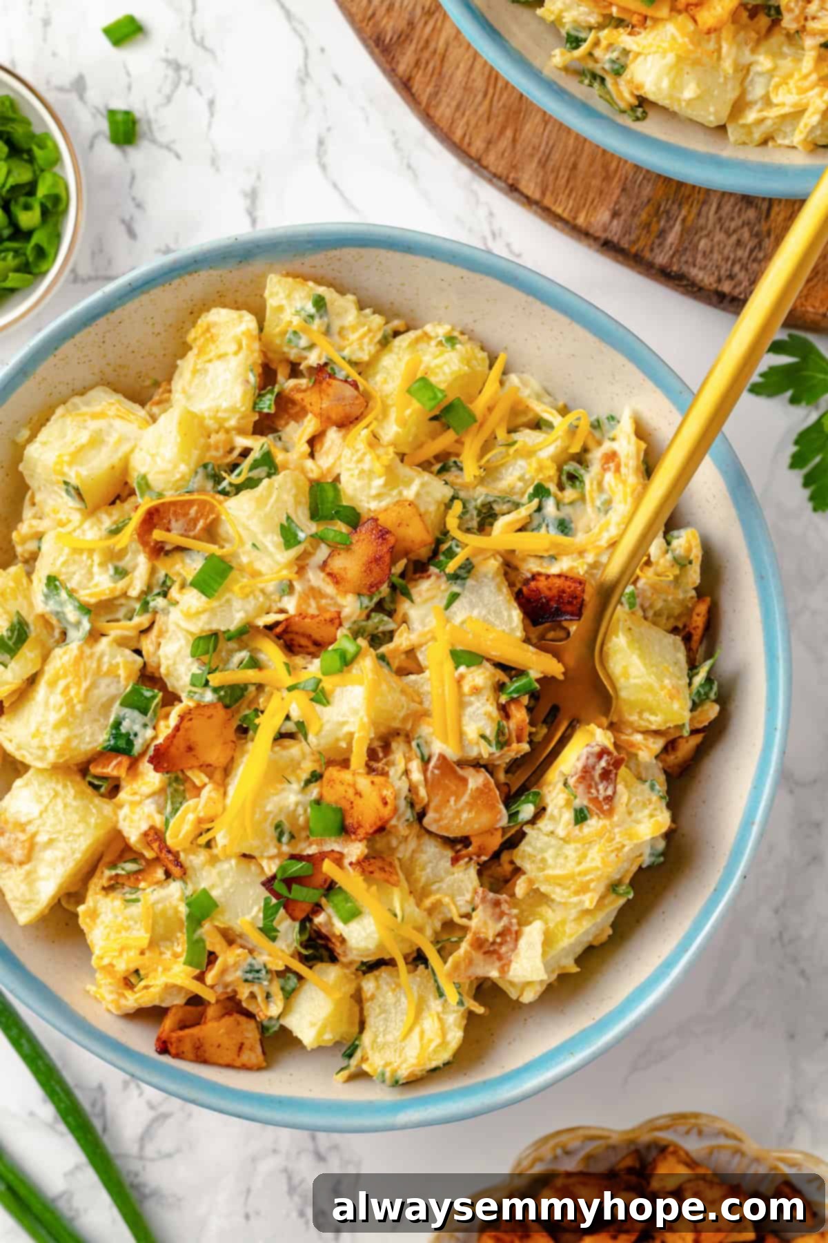 Overhead view of a generous bowl of creamy vegan loaded potato salad, garnished with fresh chives, a fork resting on the side, highlighting its rich textures and inviting toppings.