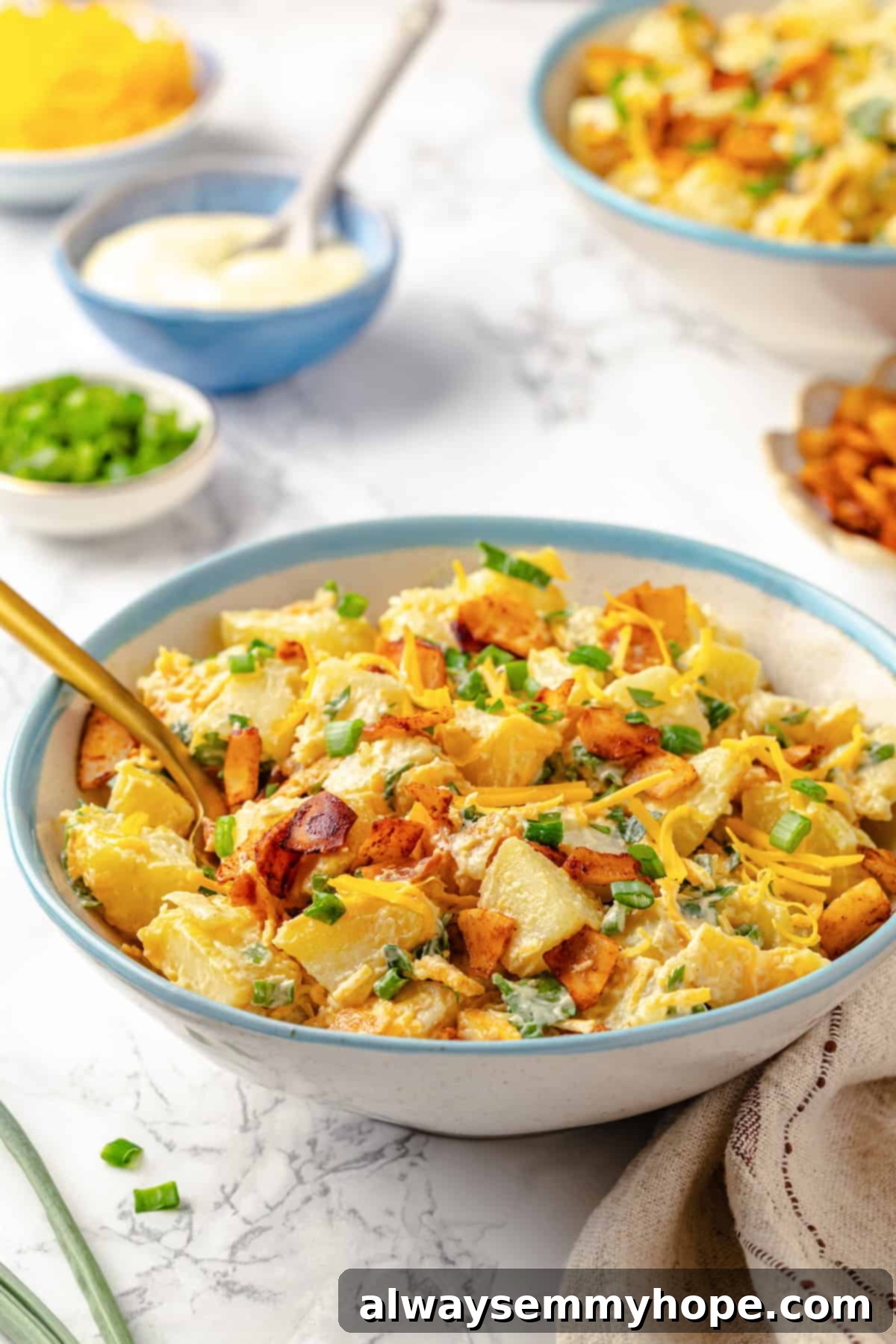 A close-up shot of a creamy bowl of vegan loaded potato salad, showcasing the visible bits of vegan cheddar, vegan bacon, and fresh green scallions.