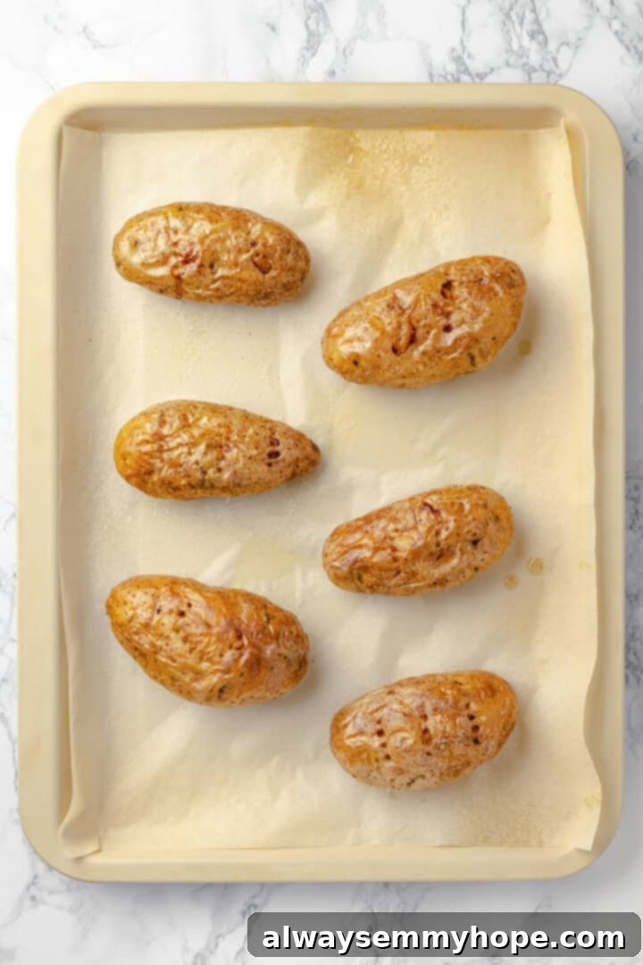 An overhead view of six whole russet potatoes, lightly oiled and seasoned, neatly arranged on a parchment-lined baking sheet, ready for baking.
