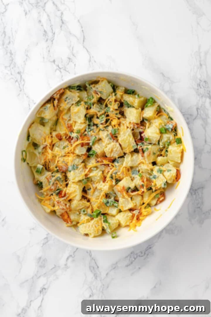 A large mixing bowl filled with the fully combined vegan loaded potato salad, showing the creamy dressing coating the potato cubes and toppings.