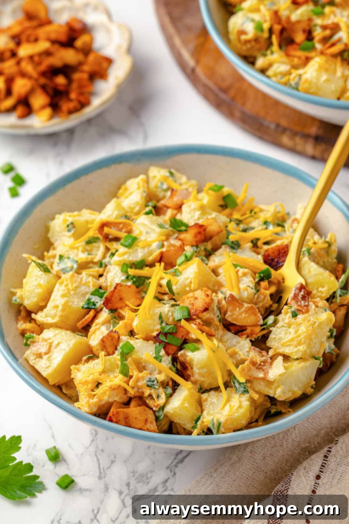 A close-up view of a bowl of creamy vegan loaded potato salad, with a fork poised to take a bite, showing the rich, inviting texture and generous toppings.