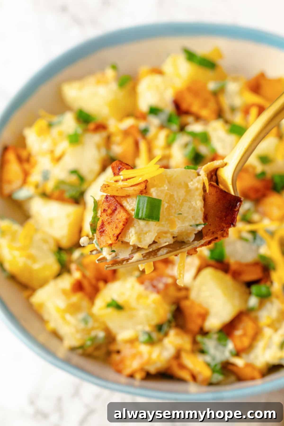 A fork lifts a generous bite of creamy vegan loaded potato salad, showing the tender potatoes, vegan bacon, and shredded vegan cheddar cheese.