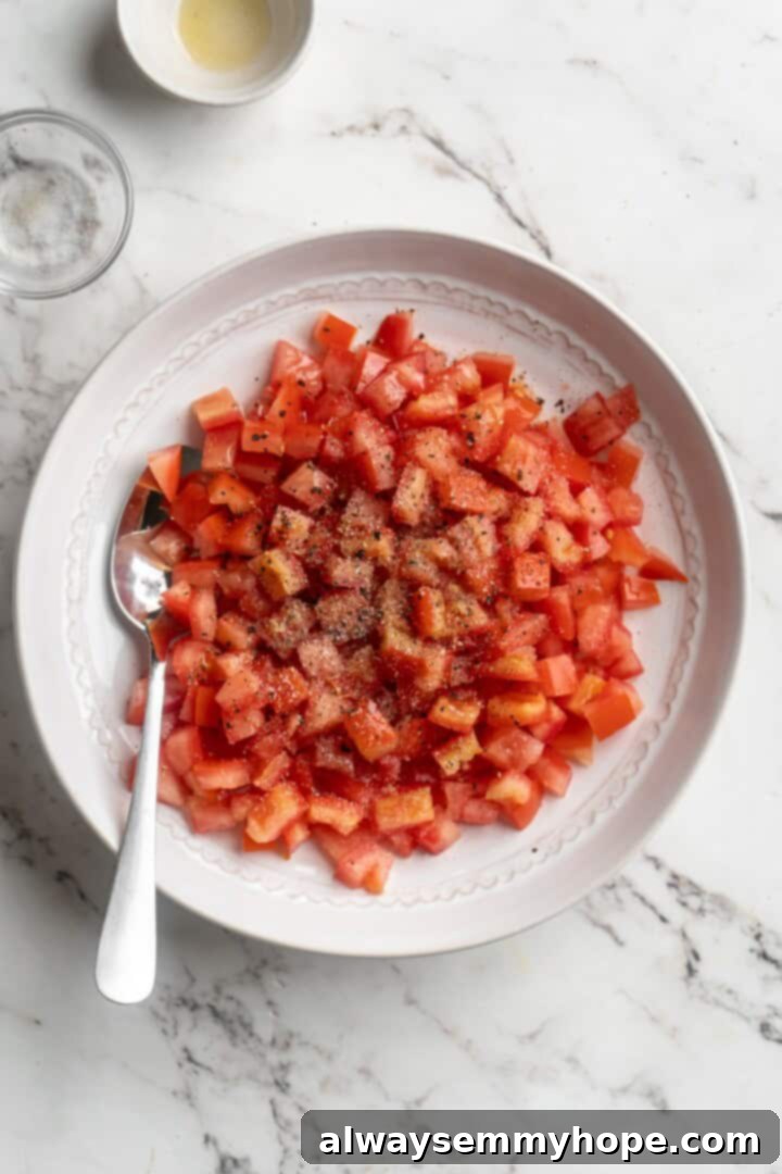 Overhead view of seasonings added to a bowl of freshly diced tomatoes, ready to be tossed for bruschetta topping.