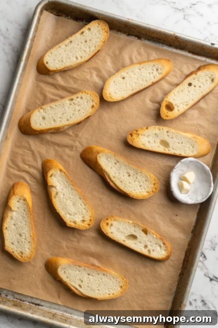 Overhead view of bread slices on a sheet pan, ready for toasting, with a clove of garlic beside them.