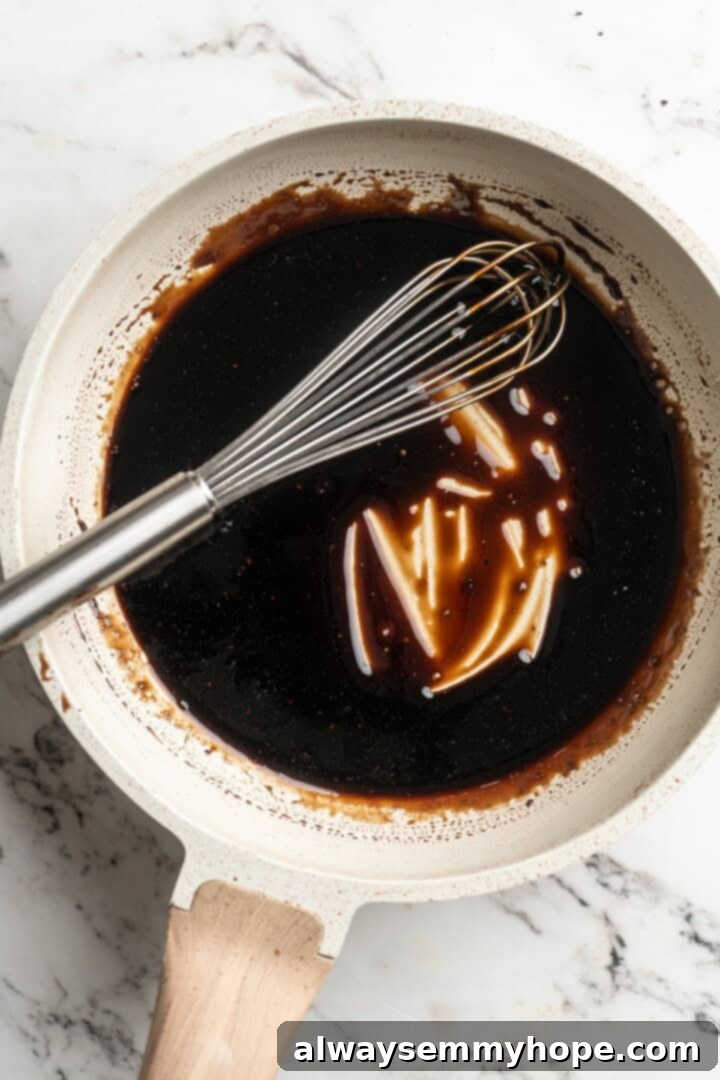 Thickened balsamic glaze in a pan with a whisk, showing the reduced, syrupy consistency.