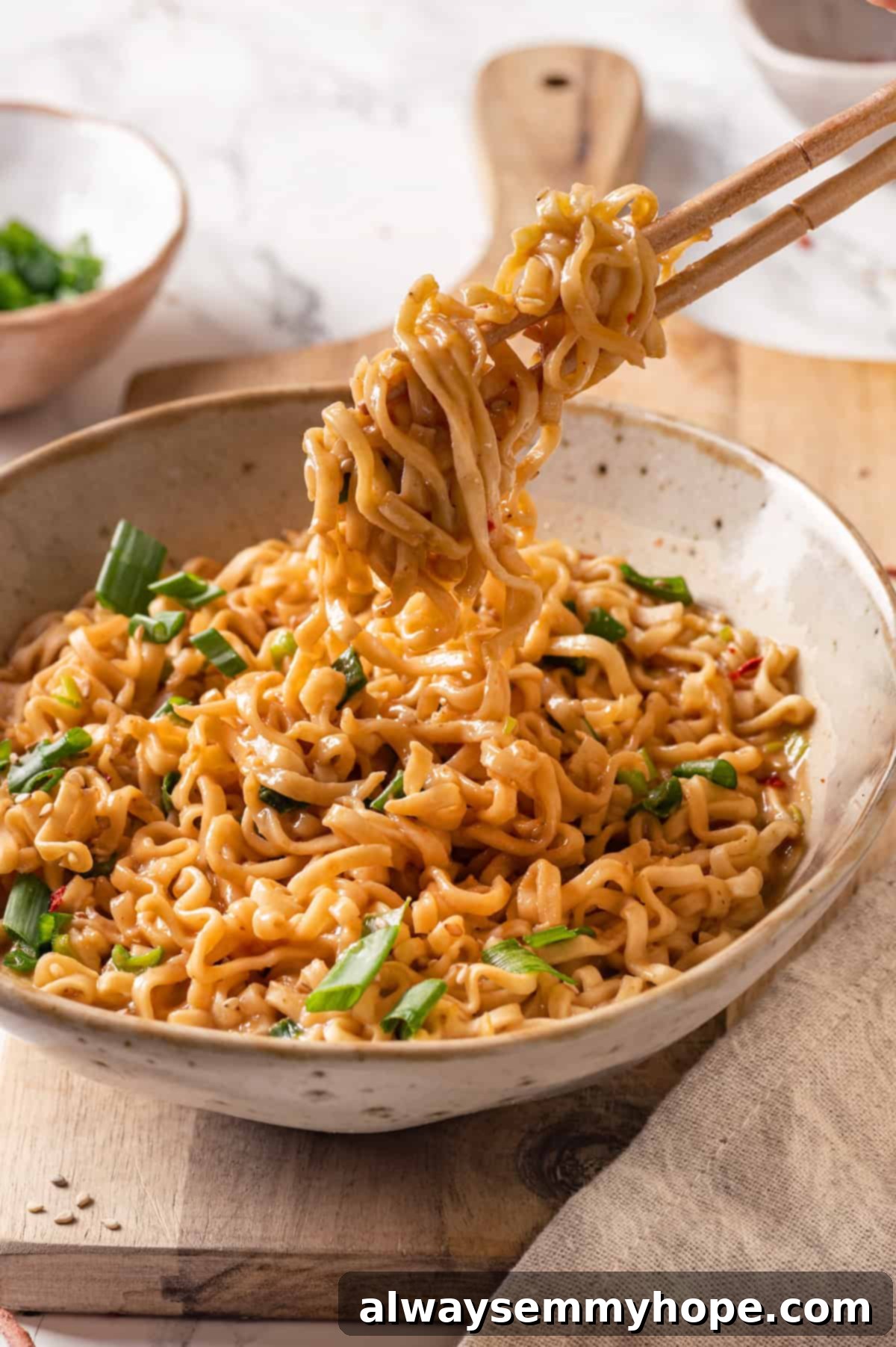 Picking up peanut butter ramen with chopsticks, showcasing the creamy sauce and fresh garnishes.