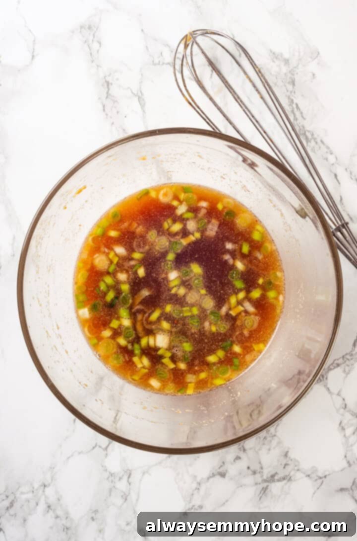 Overhead view of vegetable stock, soy sauce, sesame oil, garlic powder, red pepper flakes, and sweet chili sauce being whisked in a bowl.