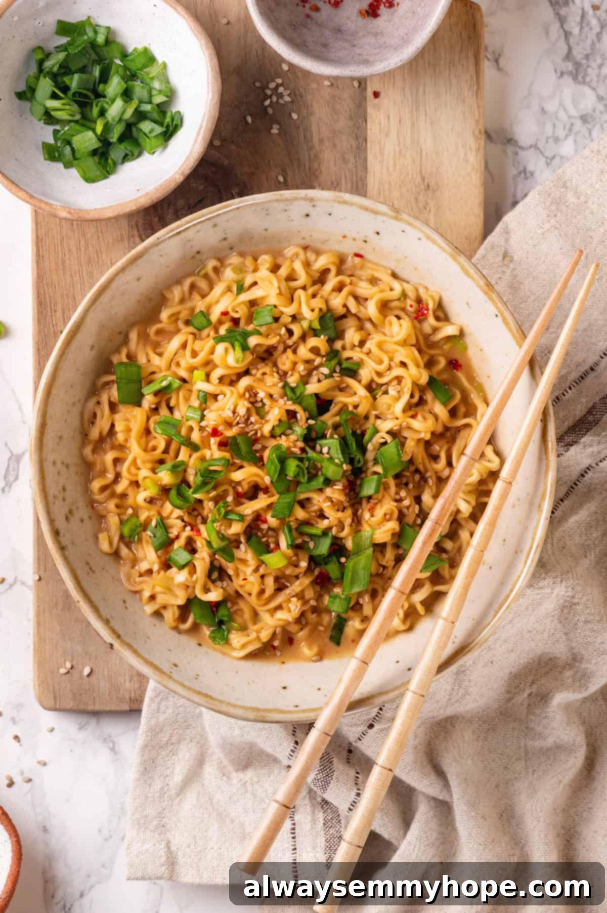 Overhead close-up of a bowl of peanut butter ramen with chopsticks, garnished with scallions and sesame seeds.
