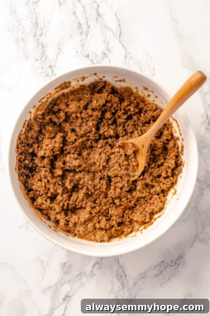 With layers of seasoned taco meat, plant-based cheese, and tortillas, this easy taco bake recipe is sure to please the whole family! Overhead view of seasoned vegan taco meat mixture in a large mixing bowl, thoroughly coated in sauce.
