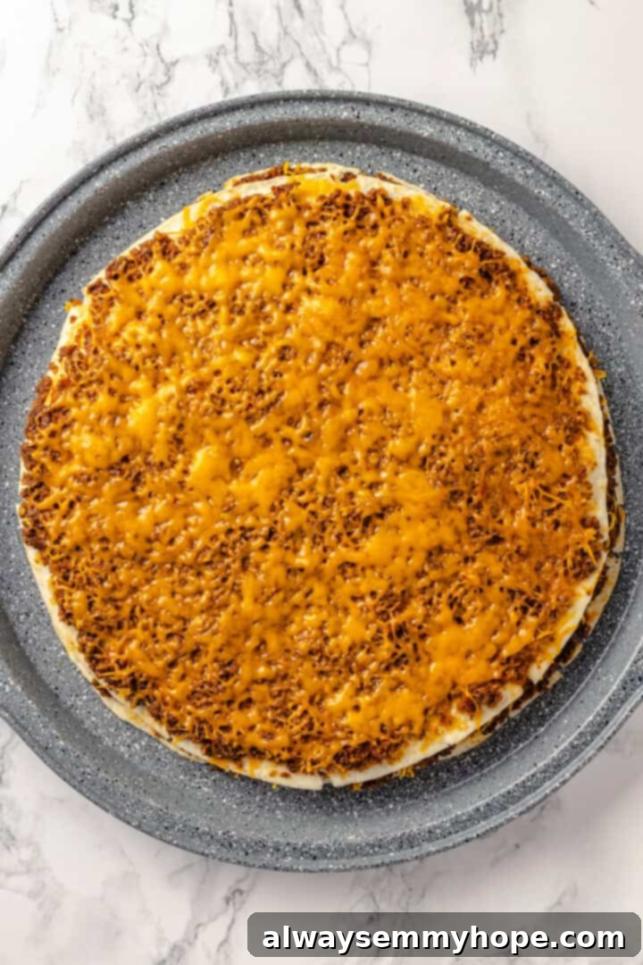 With layers of seasoned taco meat, plant-based cheese, and tortillas, this easy taco bake recipe is sure to please the whole family! Overhead view of the fully assembled vegan taco bake in a round pan, topped with a generous layer of vegan cheese, ready for baking.