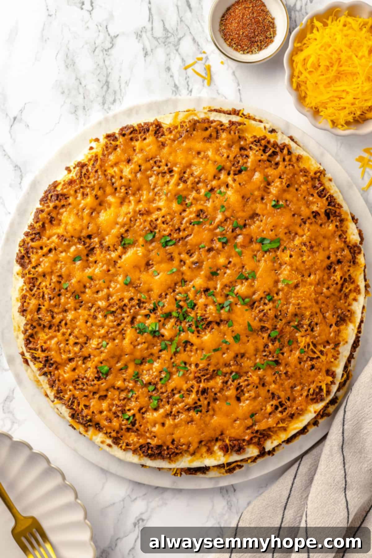 With layers of seasoned taco meat, plant-based cheese, and tortillas, this easy taco bake recipe is sure to please the whole family! Overhead view of the baked vegan taco casserole in its round pan, hot and ready to be sliced, topped with perfectly melted cheese.