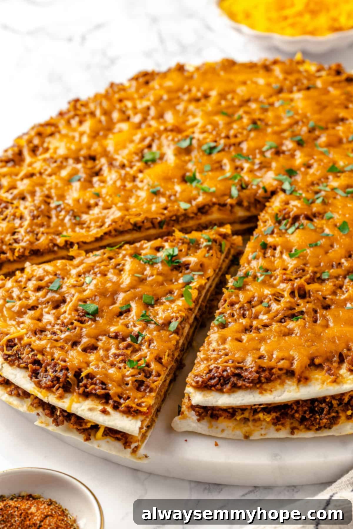 With layers of seasoned taco meat, plant-based cheese, and tortillas, this easy taco bake recipe is sure to please the whole family! A slice of vegan taco bake being lifted out of the pan with a spatula, showcasing its layers and melted cheese.