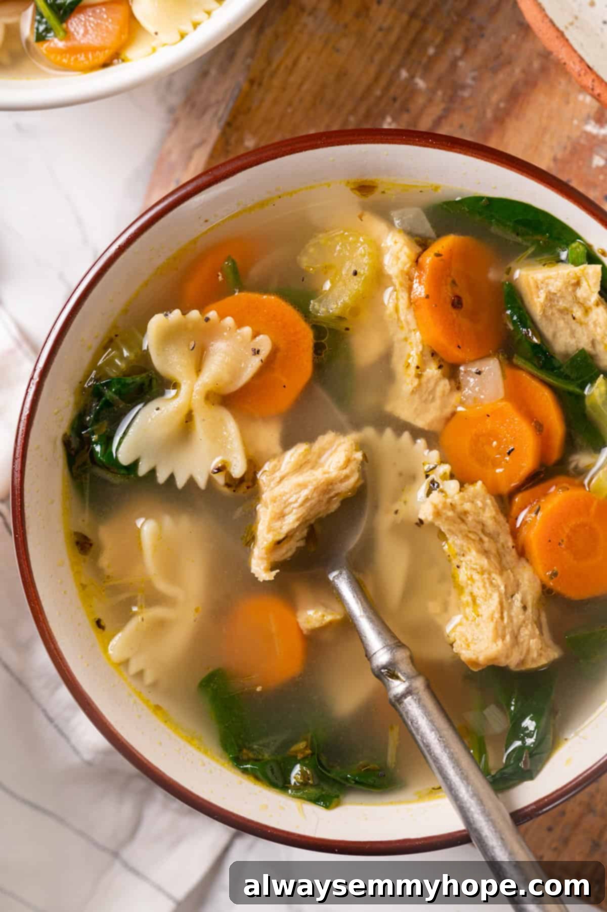 Overhead view of a steaming bowl of vegan chicken noodle soup with a spoon, ready to be enjoyed.