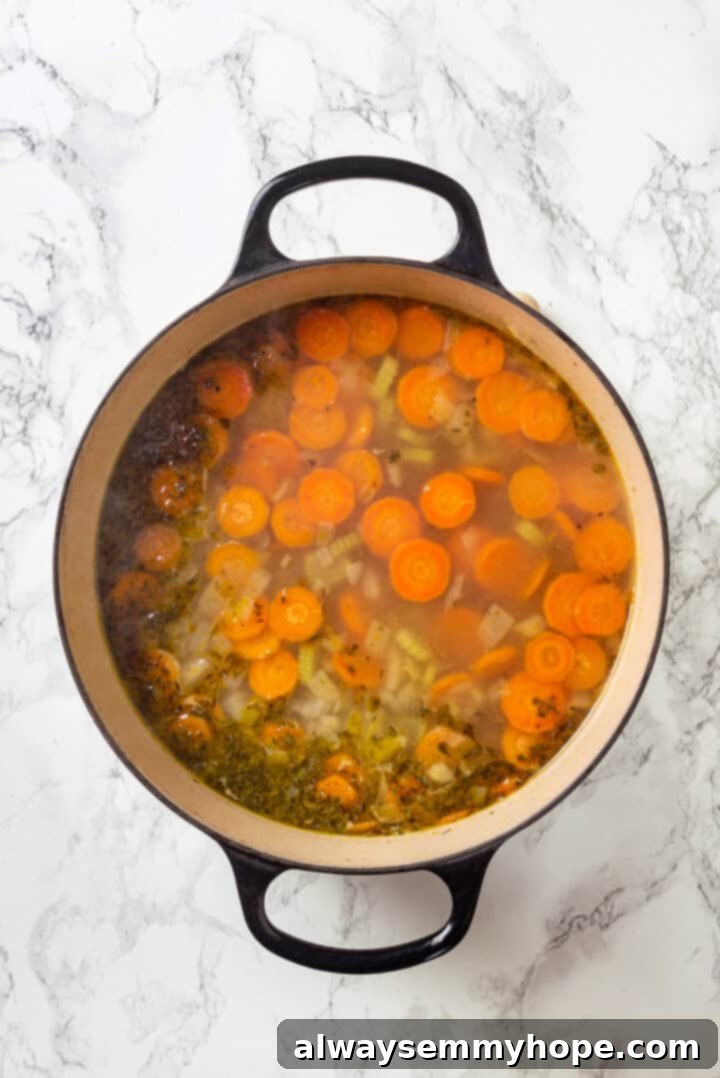 Overhead view of vegan chicken noodle soup broth simmering in a pot with vegetables before pasta is added.