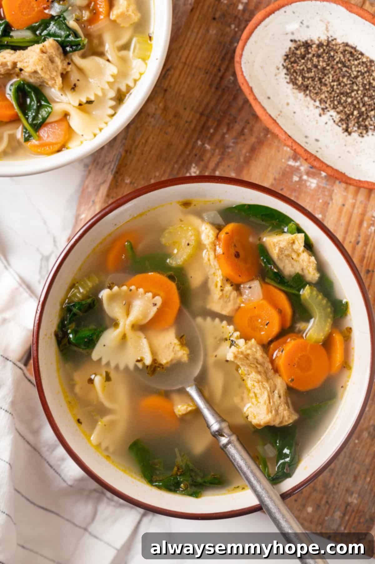 Overhead view of a steaming bowl of vegan chicken noodle soup, garnished with fresh herbs, alongside a spoon.
