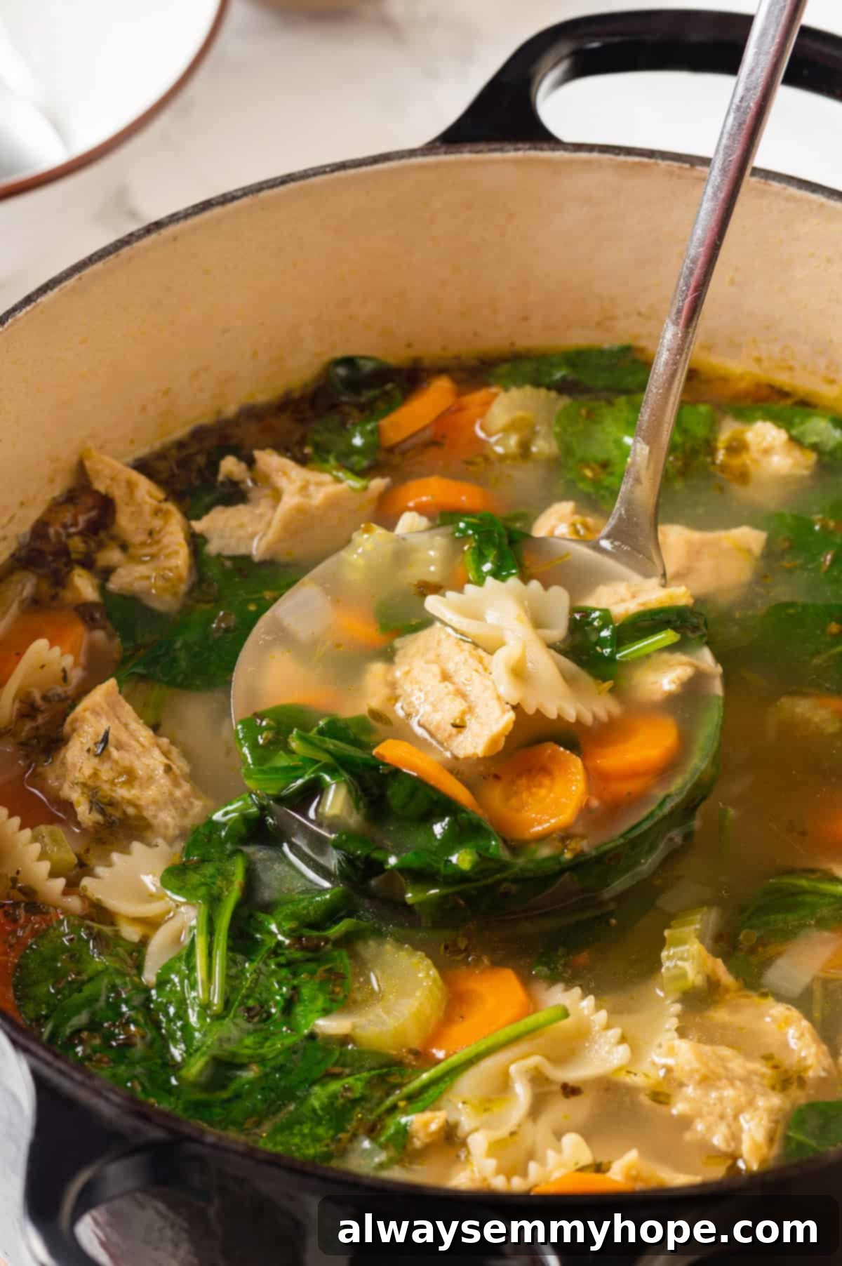 A ladleful of rich vegan chicken noodle soup being served from a large pot.