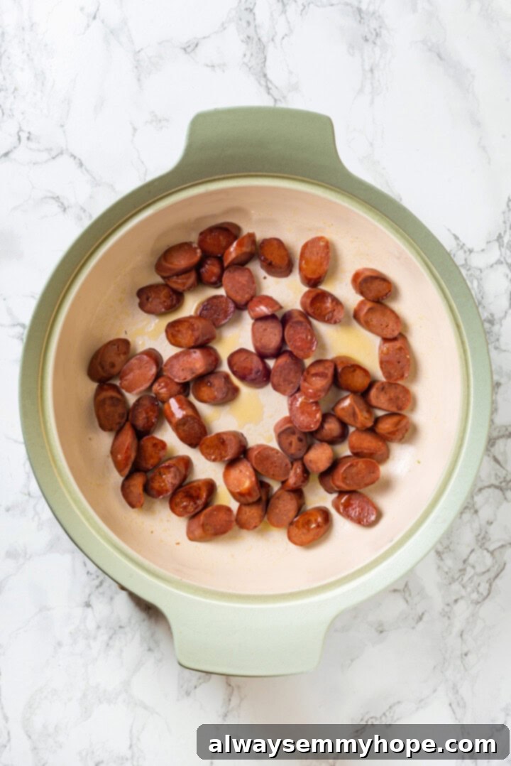 Vegan jambalaya recipe is comfort food Cajun style! With rice, veggies and plant-based sausage, this is a meal that’s flavourful and hearty. Overhead view of vegan sausage cooking in skillet, lightly browned