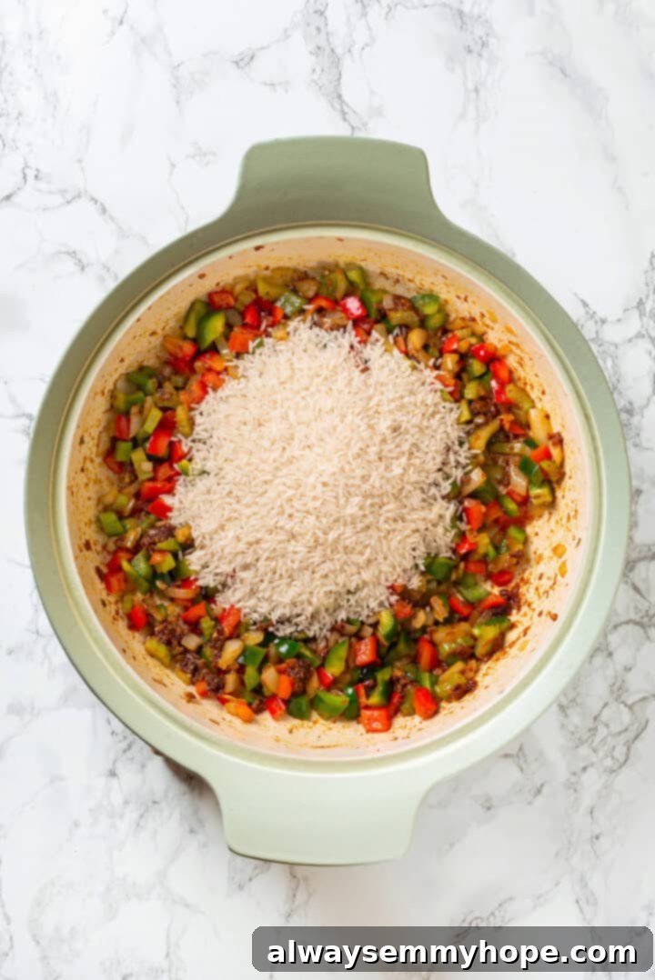 Vegan jambalaya recipe is comfort food Cajun style! With rice, veggies and plant-based sausage, this is a meal that’s flavourful and hearty. Overhead view of basmati rice added to skillet of sauteed veggies and roux