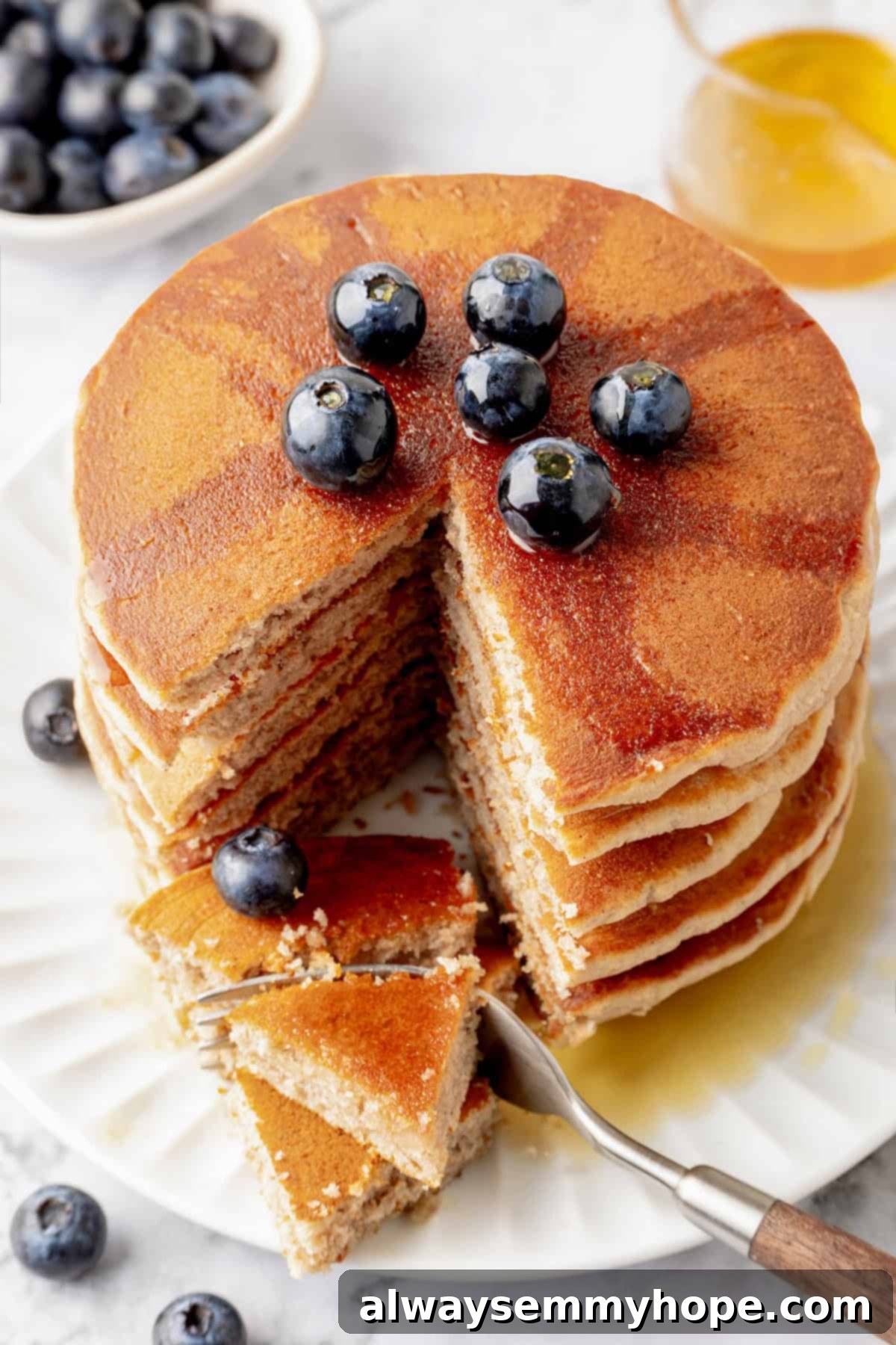 A stunning final shot of a tall stack of vegan buckwheat pancakes, drenched in maple syrup and adorned with fresh blueberries, ready to be served.