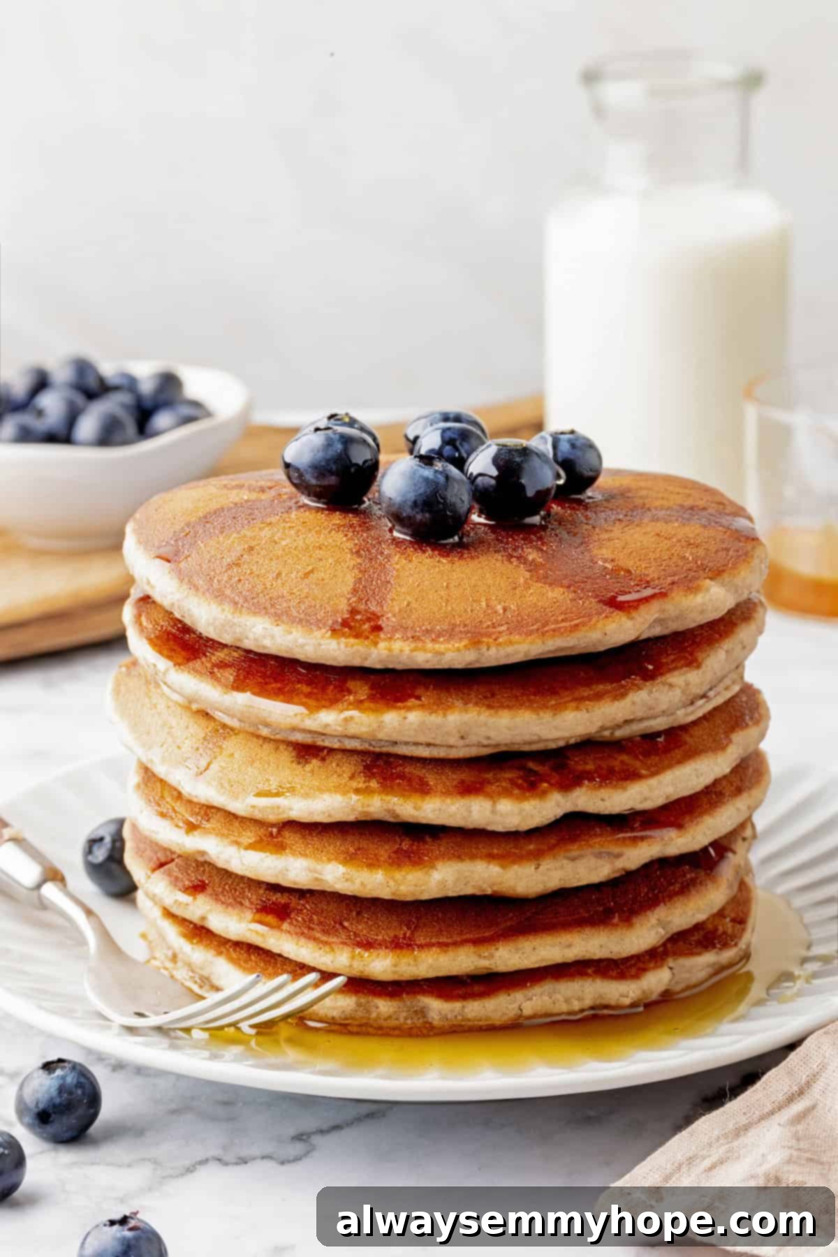 A beautiful stack of vegan buckwheat pancakes, generously topped with glistening maple syrup and fresh, vibrant blueberries