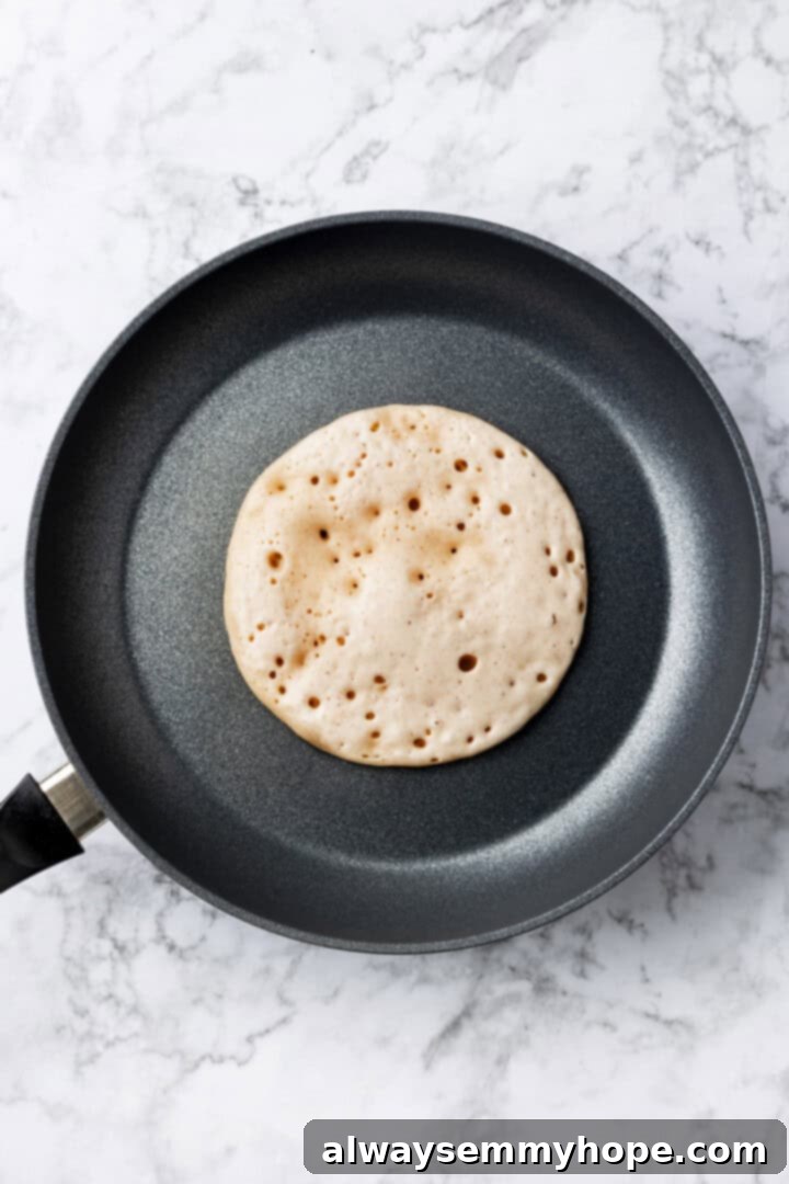 Overhead shot of a single vegan buckwheat pancake cooking in a hot skillet, with bubbles forming on the surface