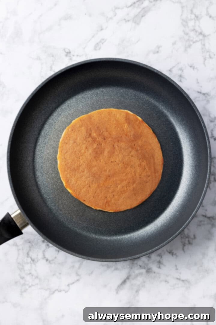 Overhead shot of a single vegan buckwheat pancake after being flipped, cooking on the second side in a skillet