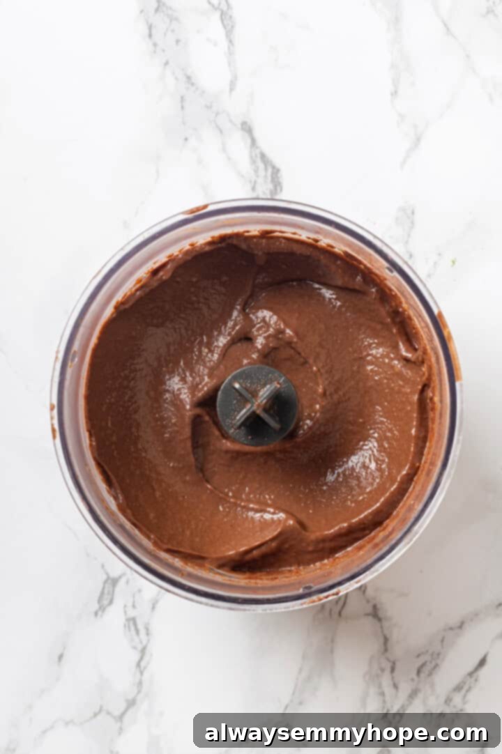 This easy avocado chocolate mousse recipe is rich, creamy, and oh-so-decadent—and you will never guess that the main ingredient is avocado! The avocado chocolate mousse mixture is blending smoothly in the food processor, showing its creamy texture.