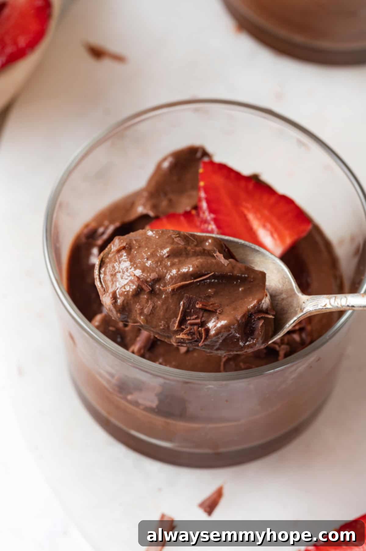 This easy avocado chocolate mousse recipe is rich, creamy, and oh-so-decadent—and you will never guess that the main ingredient is avocado! A delicious ramekin of chocolate avocado mousse with a spoon digging in, showing its perfectly creamy texture.