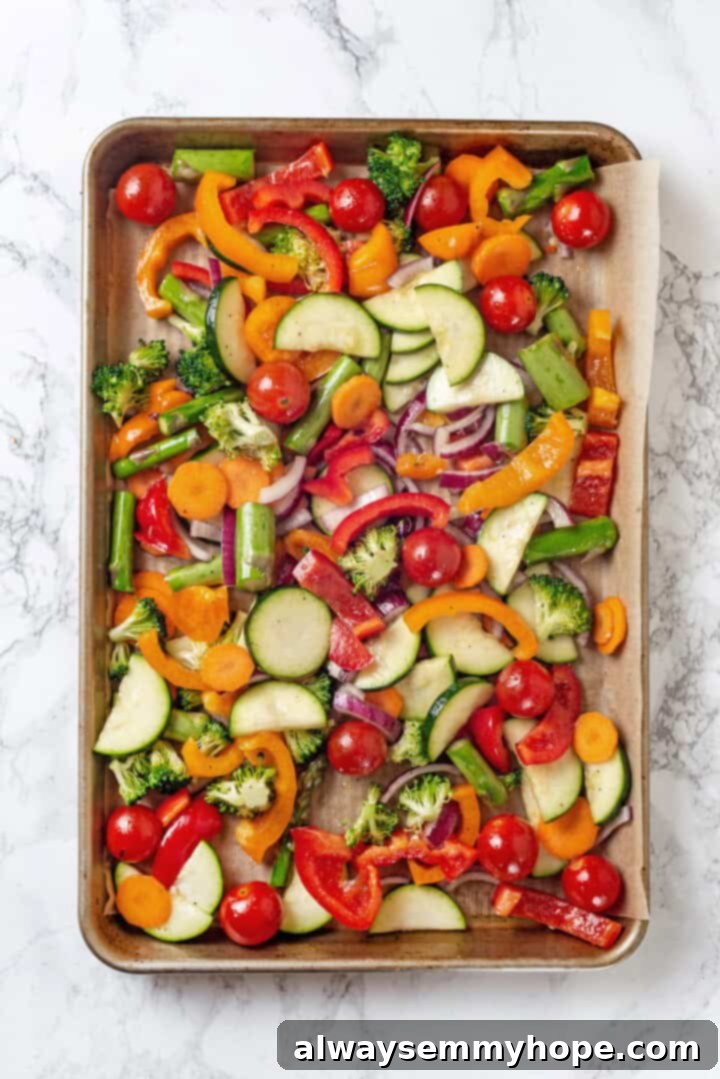 Overhead view of raw, seasoned vegetables spread on a sheet pan for roasting