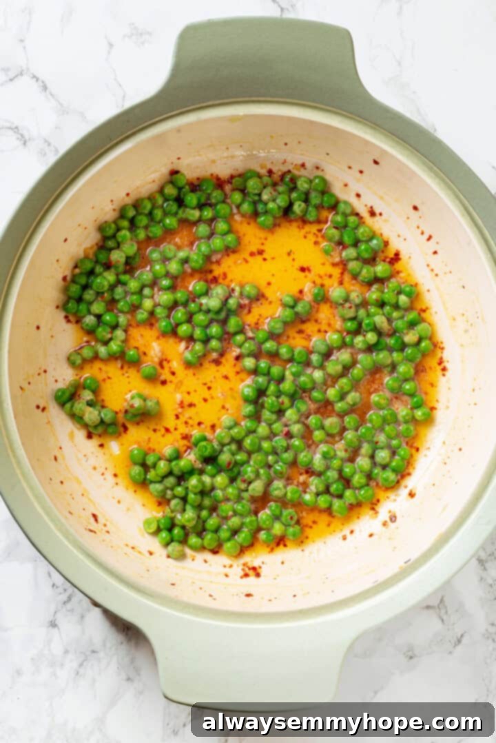 Overhead view of frozen peas, olive oil, vegan butter, and red pepper flakes in a hot skillet