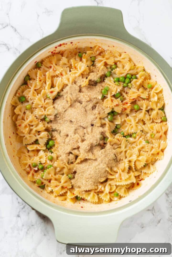 Overhead view of nutritional yeast being added to cooked pasta in a skillet with sauce