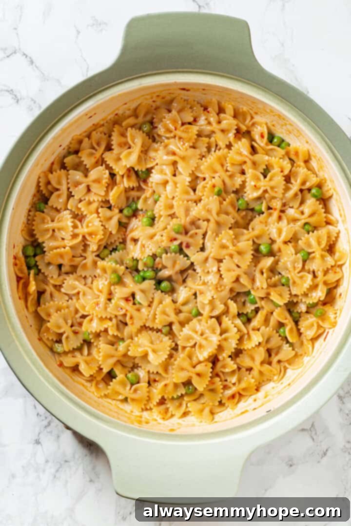 Overhead view of cooked bowtie pasta mixed with peas and a creamy sauce in a large skillet