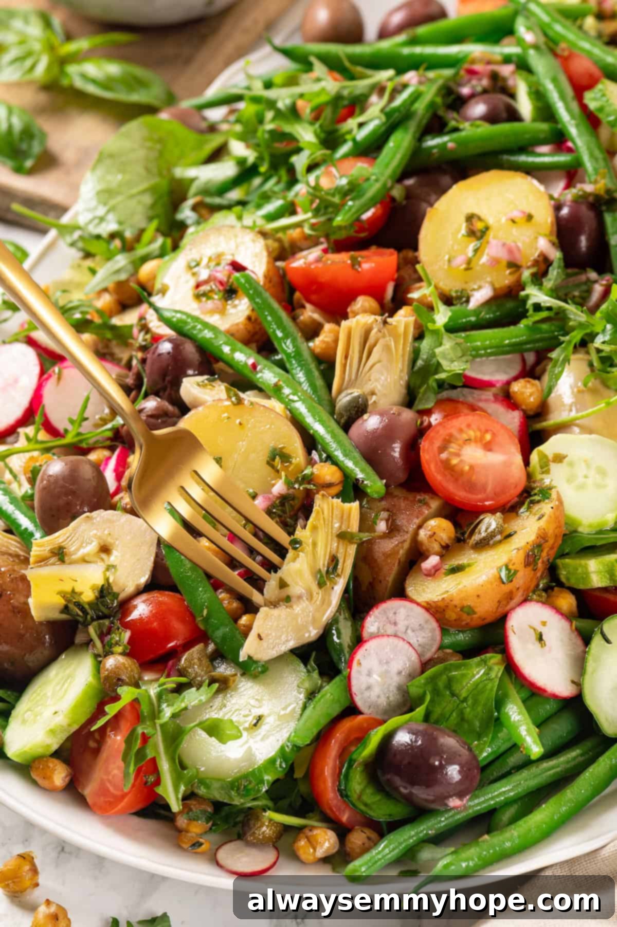 Fork piercing artichoke heart on platter of vegan nicoise salad