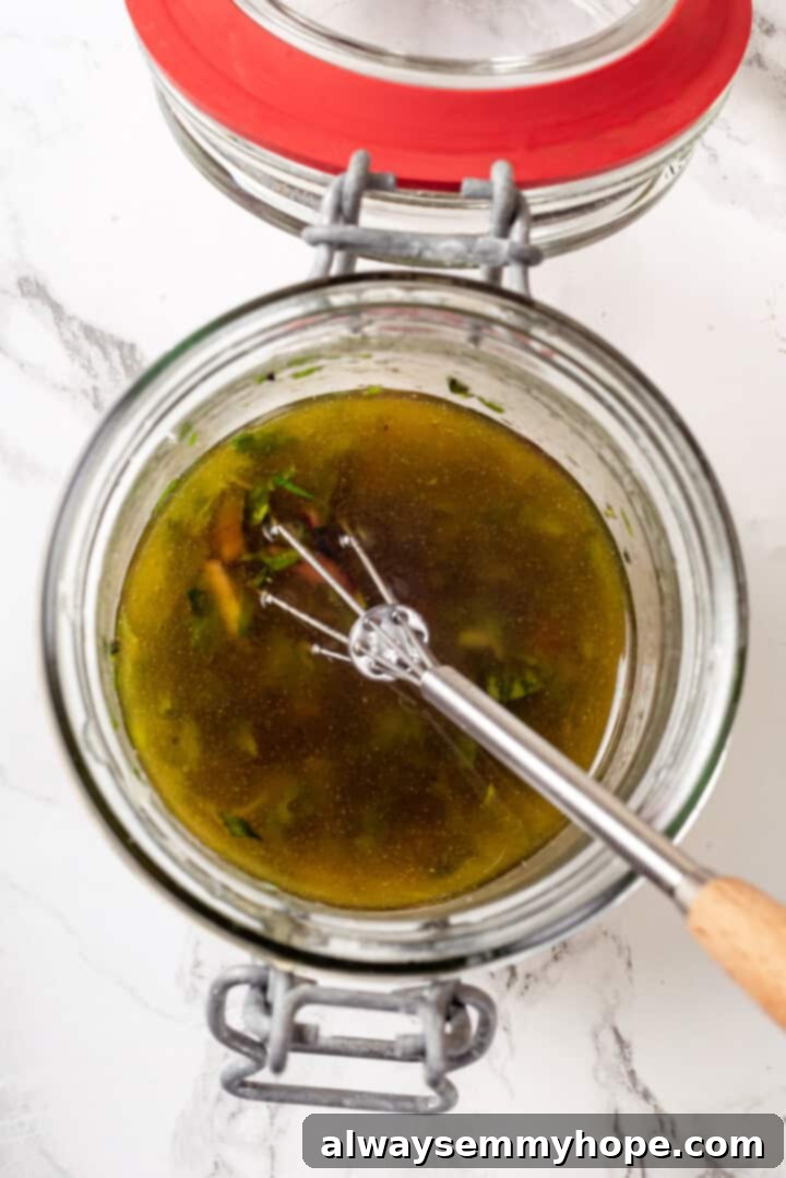 A whisk stirring a freshly made lemon vinaigrette dressing in a glass jar, ready for the vegan Nicoise salad.