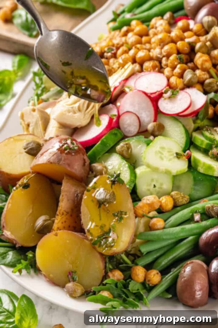 Freshly made lemon vinaigrette being drizzled over an artfully arranged vegan Nicoise salad on a large platter.