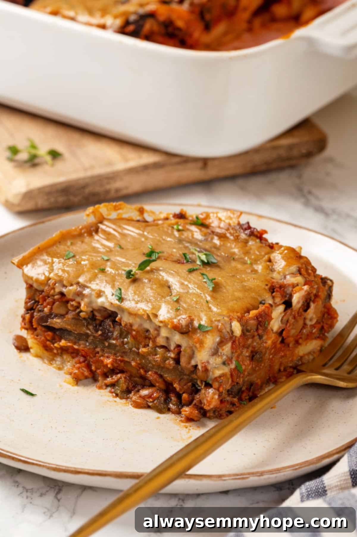 This vegan moussaka recipe has all the flavour of the classic Greek eggplant dish, but with tender lentils and mushrooms replacing the meat! Portion of vegan moussaka on plate with fork