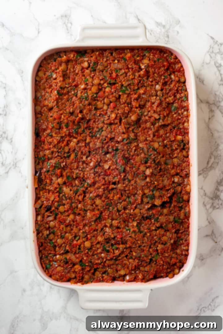 This vegan moussaka recipe has all the flavour of the classic Greek eggplant dish, but with tender lentils and mushrooms replacing the meat! Overhead view of lentils and sauce added to vegan moussaka