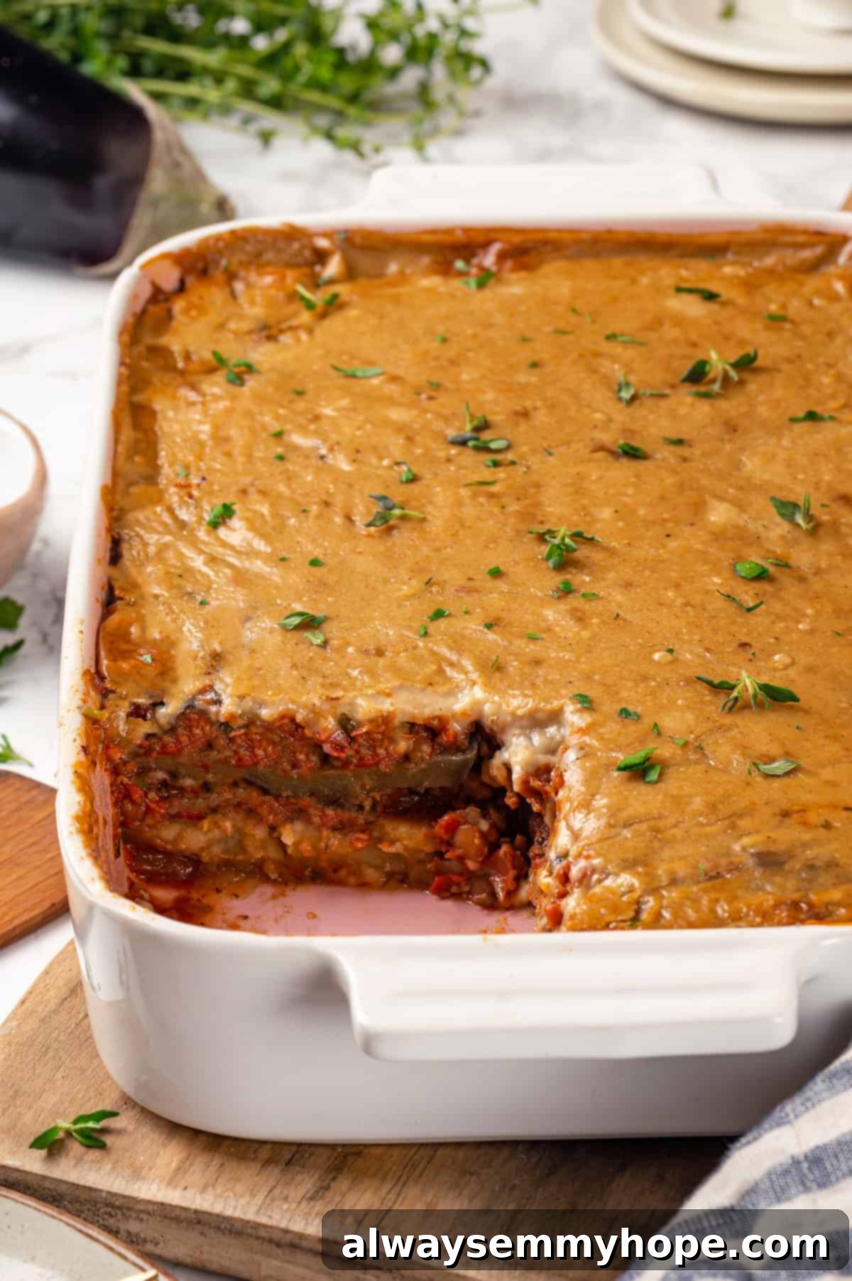 This vegan moussaka recipe has all the flavour of the classic Greek eggplant dish, but with tender lentils and mushrooms replacing the meat! Baking dish of vegan moussaka with portion removed