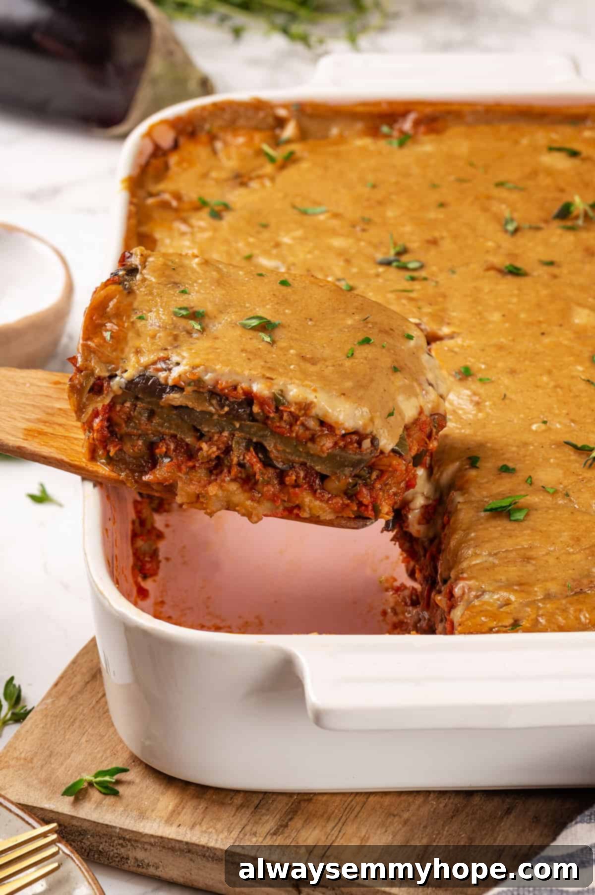 This vegan moussaka recipe has all the flavour of the classic Greek eggplant dish, but with tender lentils and mushrooms replacing the meat! Removing portion of vegan moussaka from baking dish