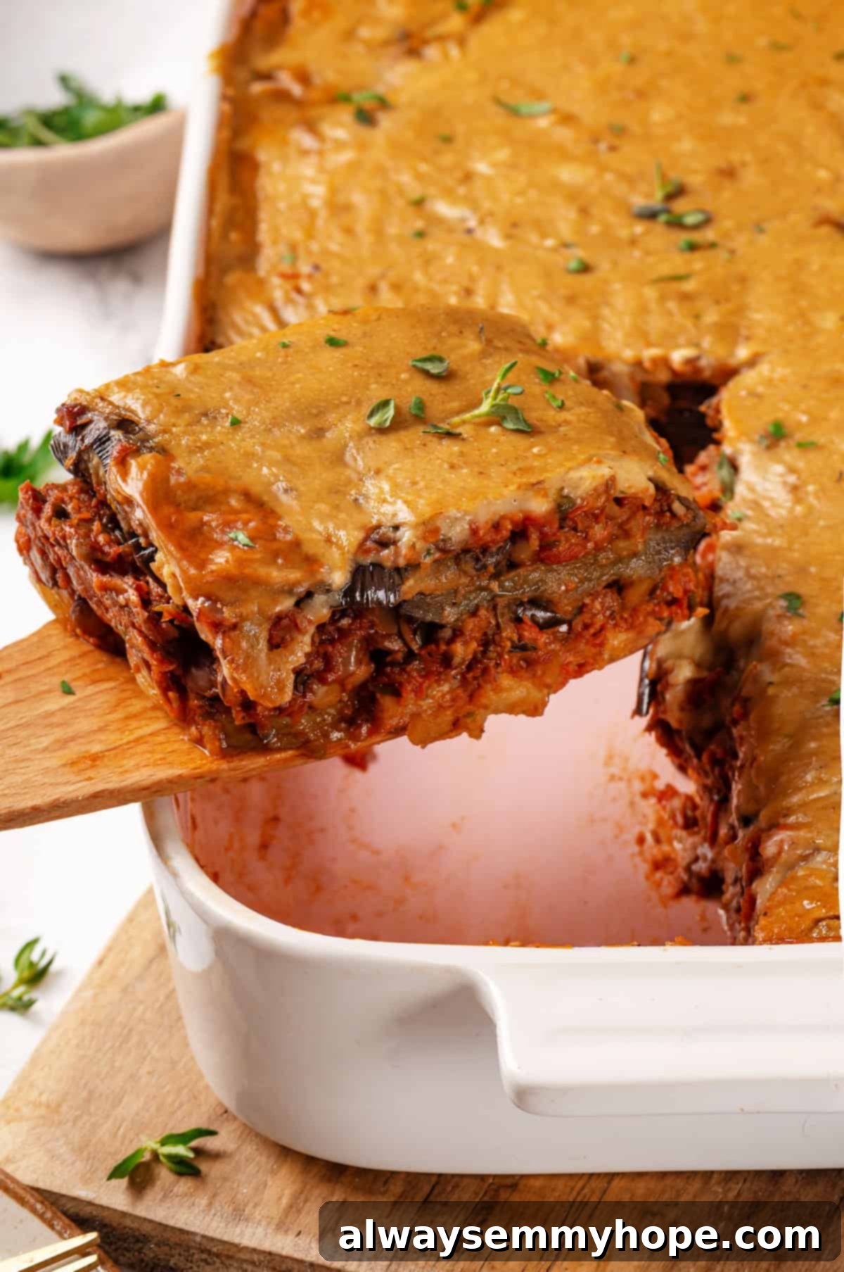 This vegan moussaka recipe has all the flavour of the classic Greek eggplant dish, but with tender lentils and mushrooms replacing the meat! Taking vegan moussaka portion out of pan
