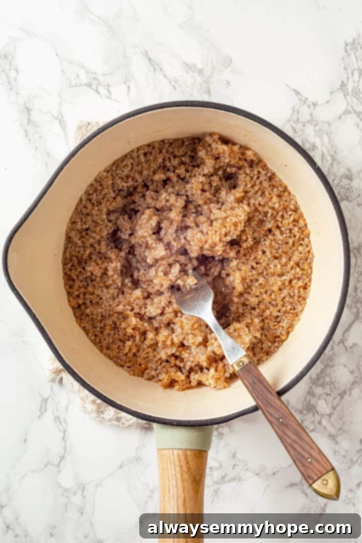Overhead view of cooked bulgur in saucepan, fluffed with a fork
