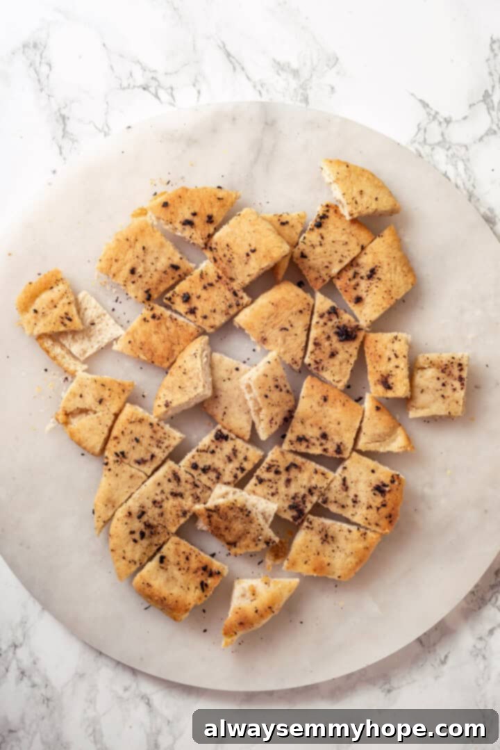 Crispy, golden-brown pita croutons, torn into bite-sized pieces, displayed on a marble surface. Golden brown pita chips on a marble board, ready for the salad