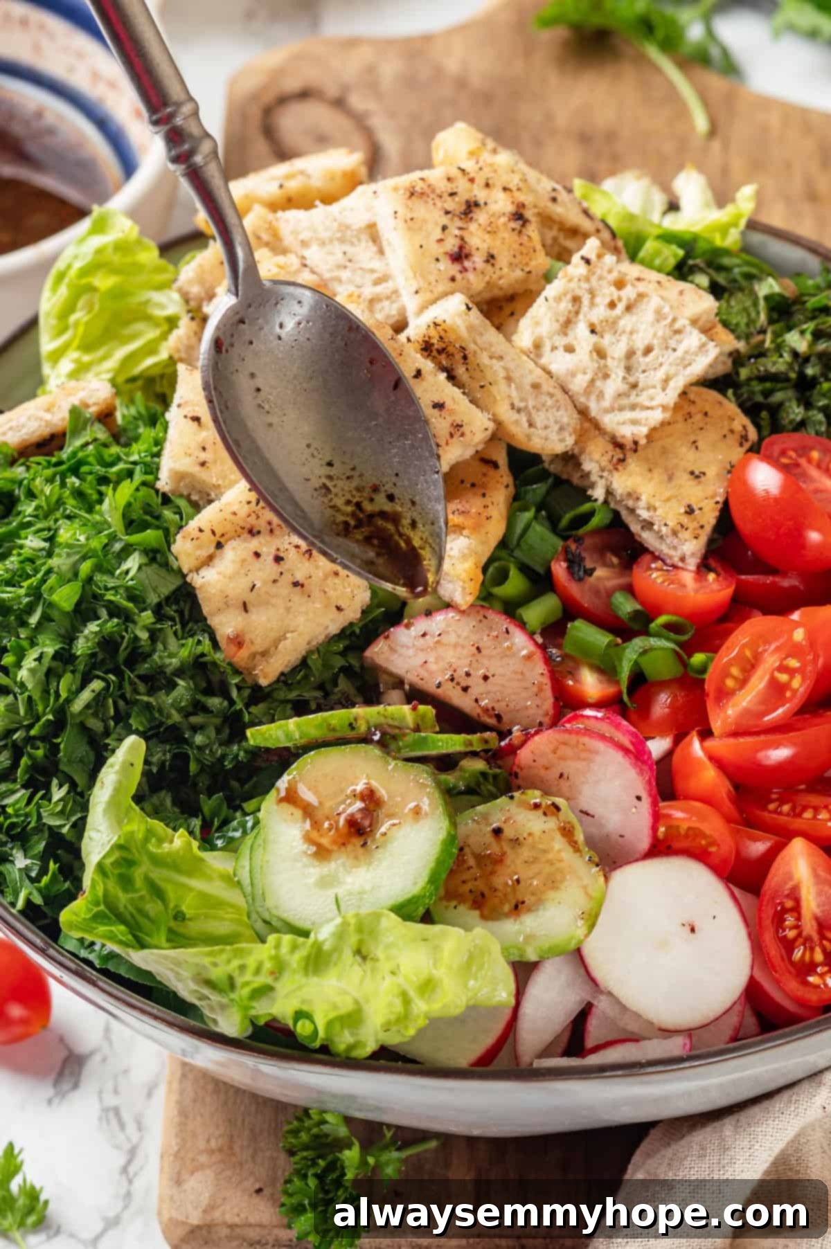 A close-up shot of the flavorful lemon-sumac dressing being drizzled over the freshly assembled Fattoush salad. Drizzling dressing onto an assembled bowl of fattoush salad