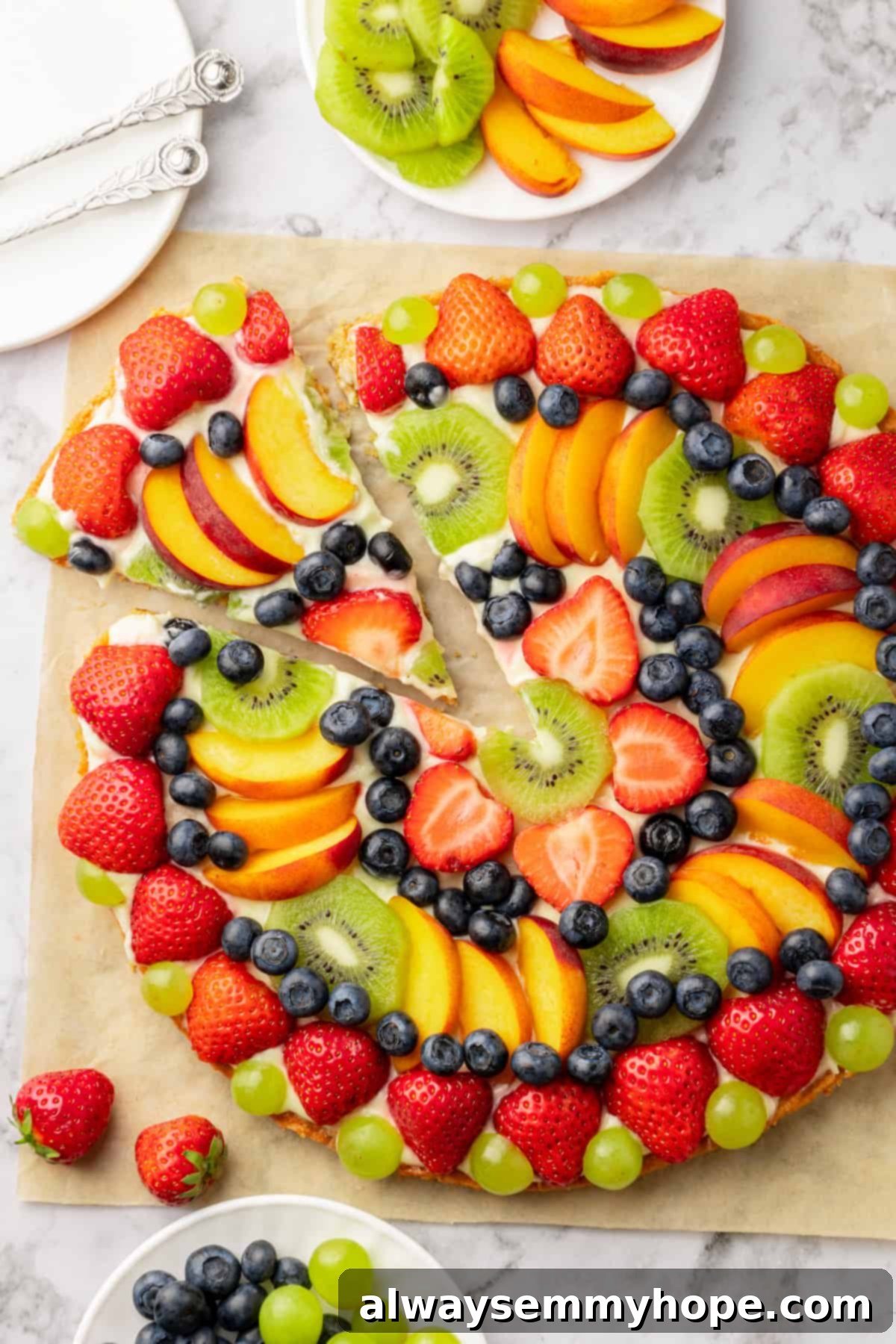 Overhead view of whole fruit pizza on parchment with piece cut and pulled away
