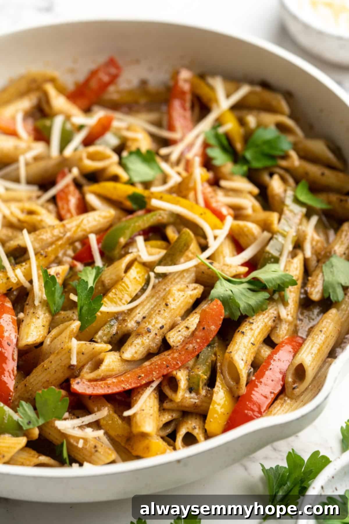 Close-up of a skillet filled with colorful Rasta Pasta, showcasing penne, bell peppers, and creamy sauce, garnished with fresh herbs.