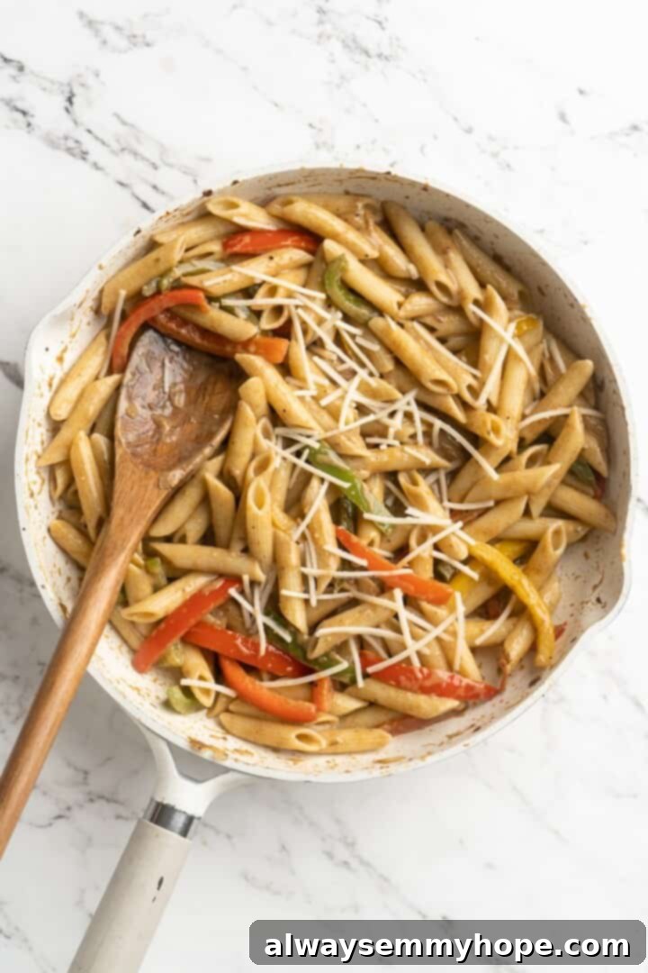 Overhead view of vegan cheese shreds being stirred into the Rasta Pasta in a skillet.
