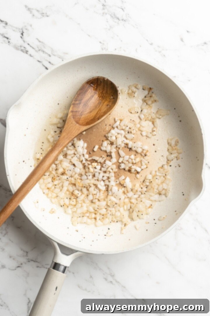 Overhead view of diced white onions softening in hot oil in a skillet.
