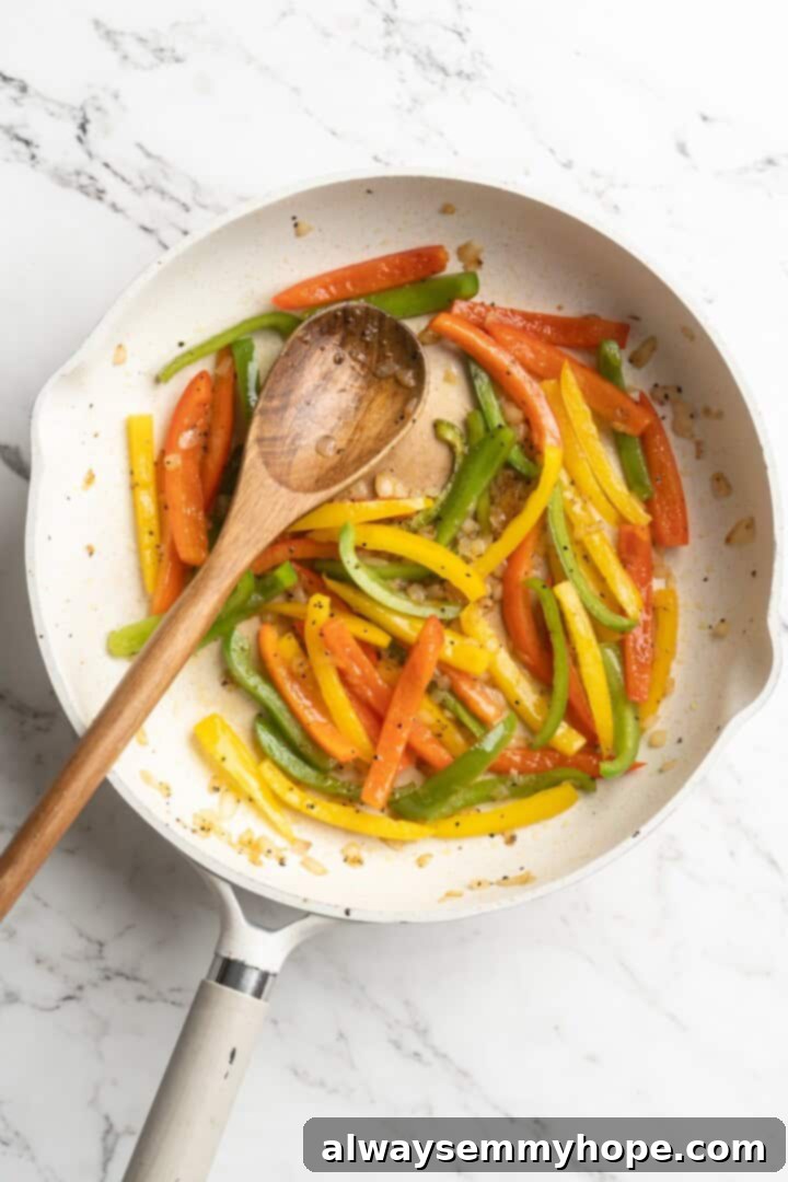 Overhead view of red, yellow, and green bell peppers sautéing in a skillet.